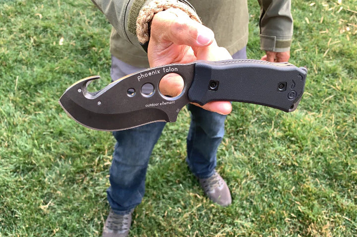 Person holding a black folding knife with grass in the background