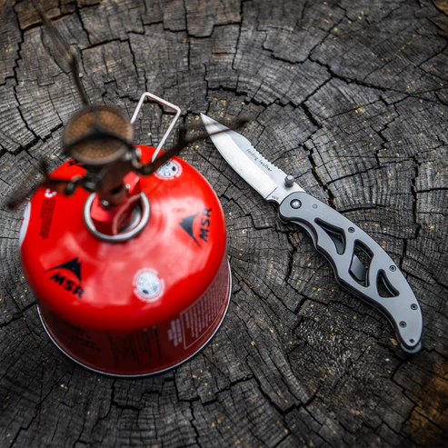 Red MSR gas canister and a folding knife on a wooden surface