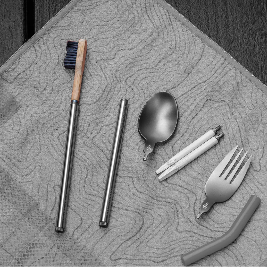 Set of reusable utensils including a brush, straws, spoon, and fork on a textured surface.